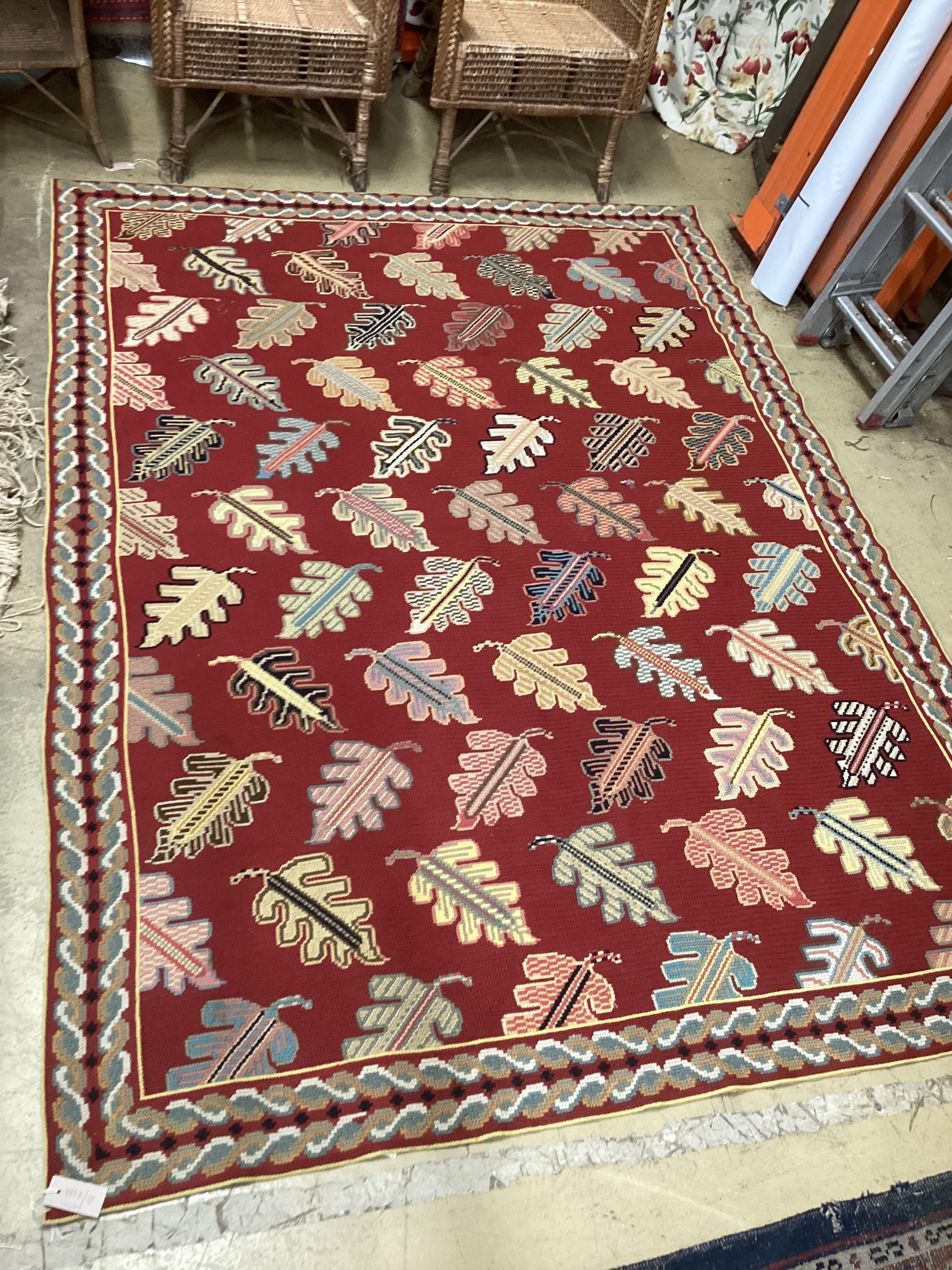 A Portuguese polychrome red ground rug woven with stylised leaves 236cm x 170cm.